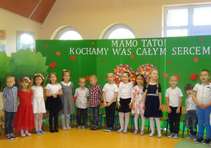Dzieci stoją na tle dekoracji na Dzień Rodziny, śpiewają piosenkę.